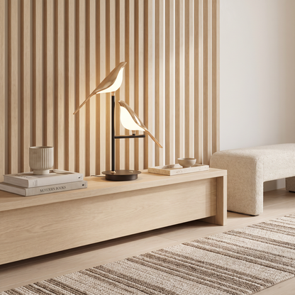 Avelle gold bird table lamp lit on an oak console in an entry hall