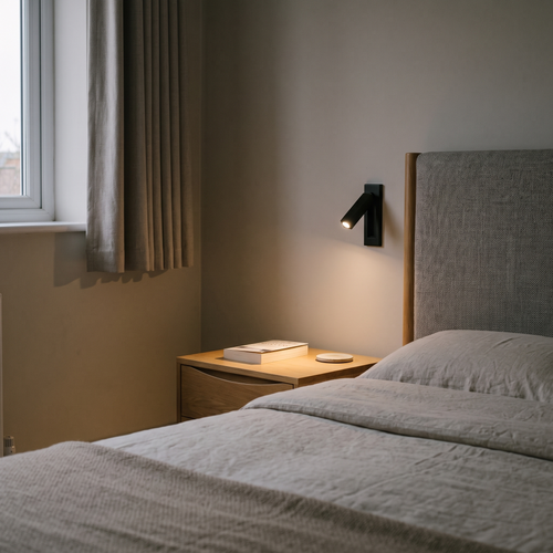 Lorenzo flush bedside reading light – matt black, lit beside a bed