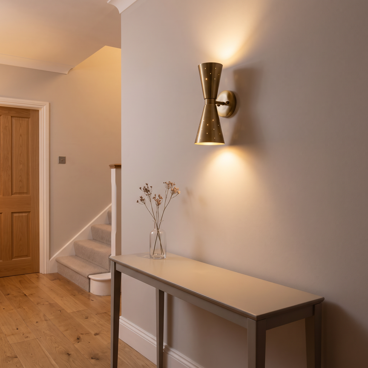 Stellan brass hourglass wall light – glowing in a hallway