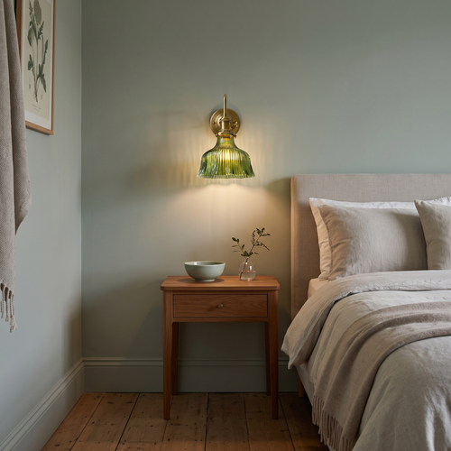 Fiorella green glass flower wall light – glowing beside a bed
