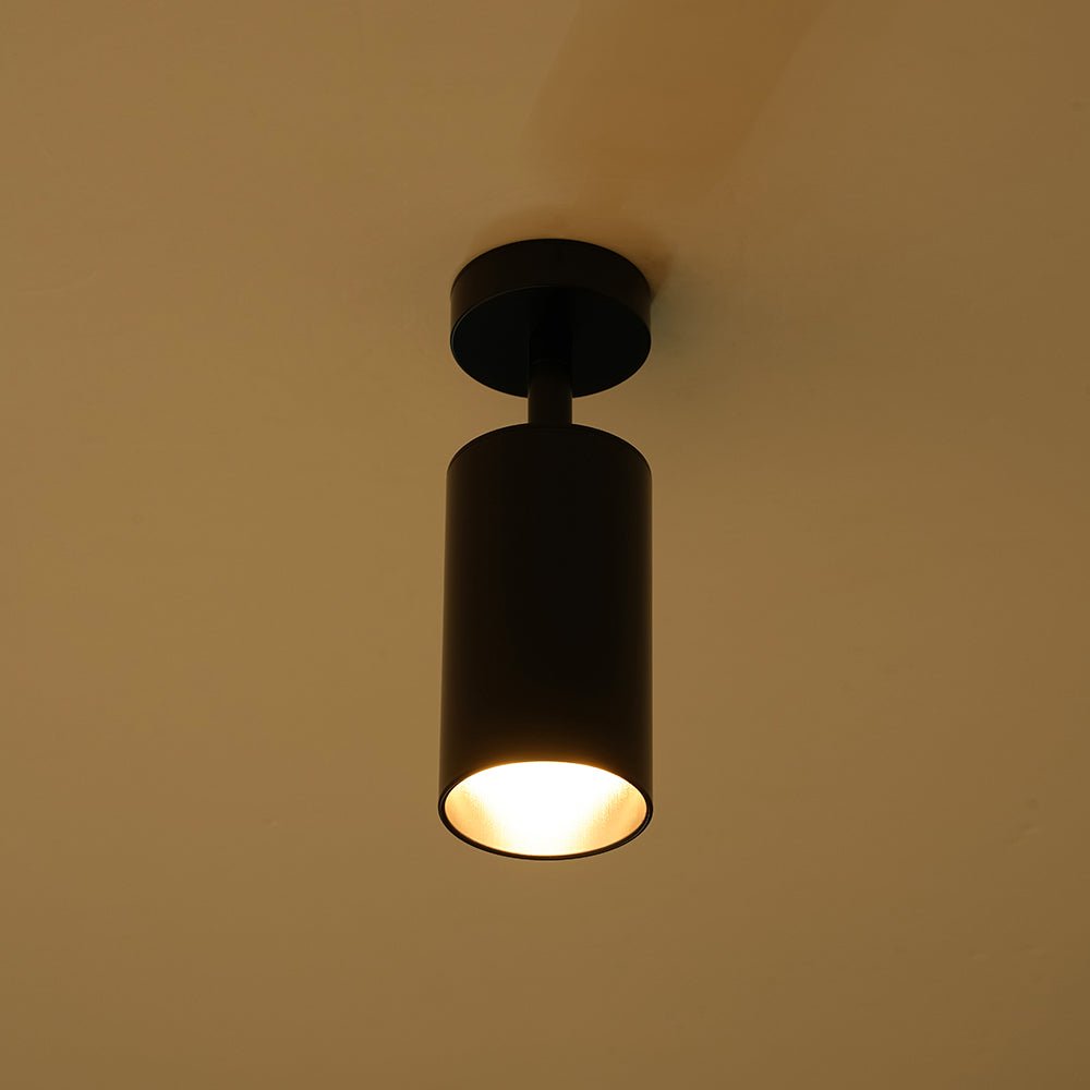 Remy adjustable spot ceiling light – in black, lit on a warm background