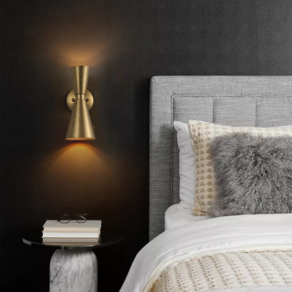 Stellan hourglass wall light – in brass, lit on a dark wall