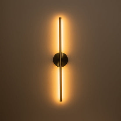 Sebastian linear LED wall light – in brass, lit on a brown wall