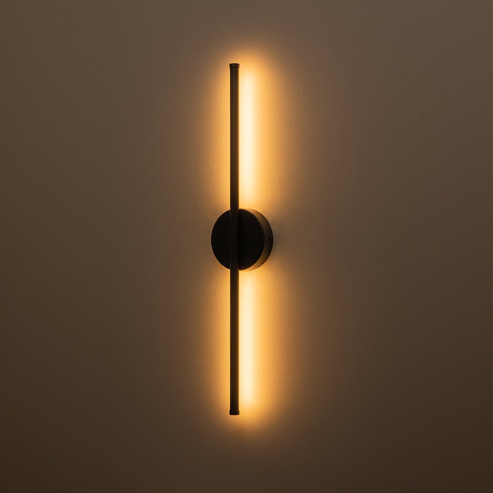 Sebastian linear LED wall light – in black, lit on a brown wall