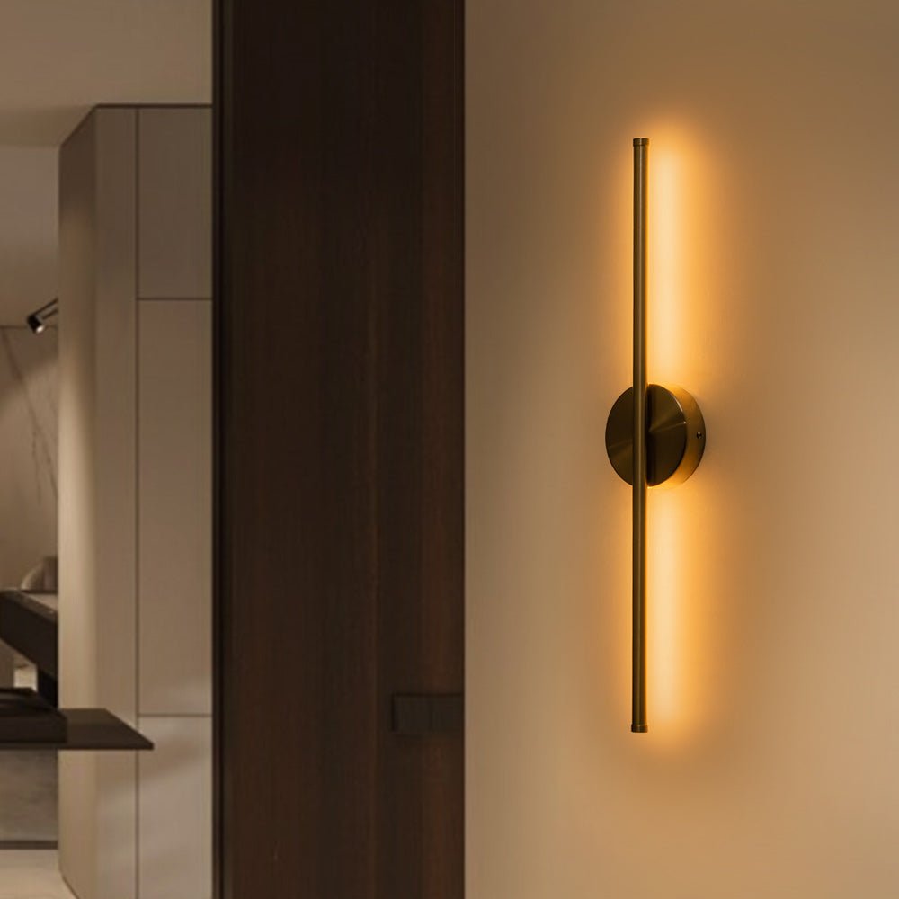 Sebastian linear LED wall light – in brass, lit on a dark wall