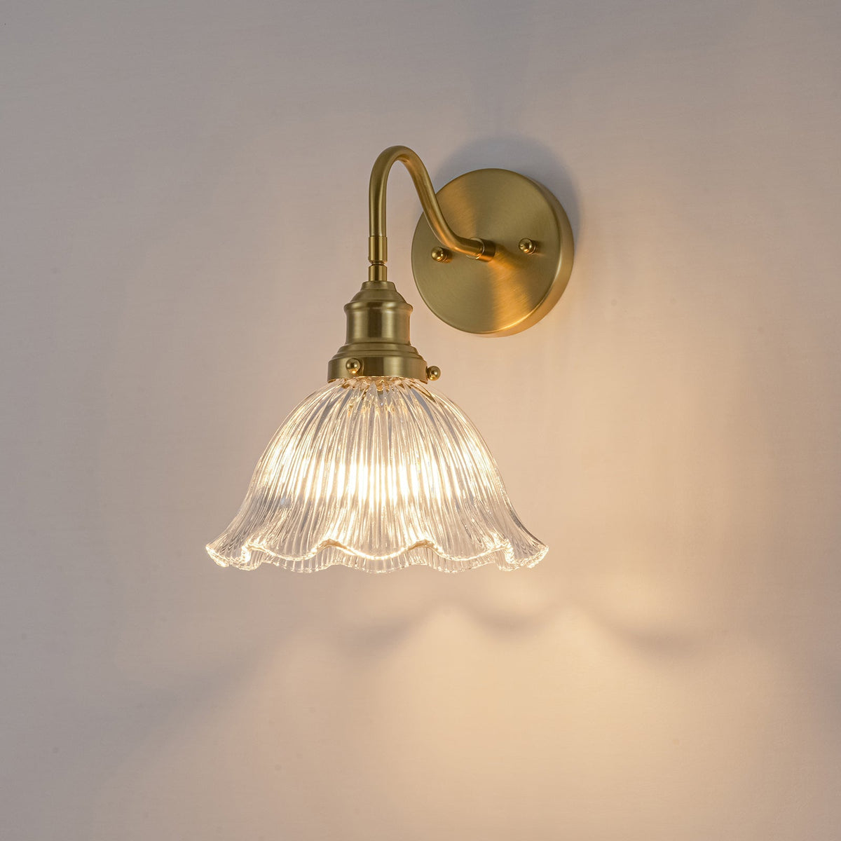 Fiorella flower wall light – in clear glass, lit on a wall